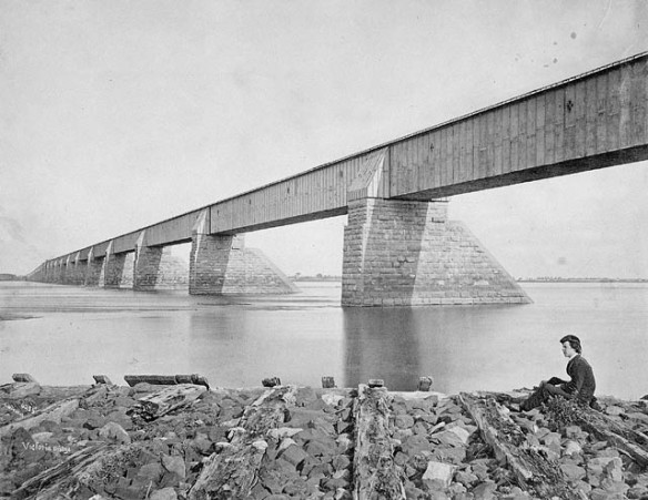 Photographie noir et blanc du pont Victoria de Montréal, avec une jeune femme assise sur un rocher au premier plan.