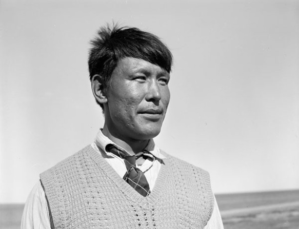 Photographie noir et blanc prise de près d’un homme Inuit portant un veston et une cravate debout à l’extérieur. 