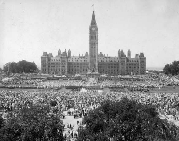 Photo noir et blanc montrant la façade avant de l’édifice du Centre. La foule se masse sur la Colline du Parlement.
