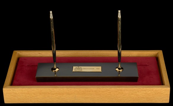 Deux stylos noir et or debout sur un socle noir et or posé sur un bloc en velours et présenté dans un coffret en bois.