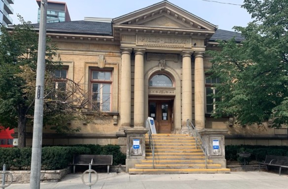 Photo couleur d’un édifice beige doté d’une entrée flanquée de colonnes et d’un fronton surplombant la porte d’entrée. Un seul escalier mène au bâtiment. Les mots « Public Library » sont gravés au-dessus de l’entrée.